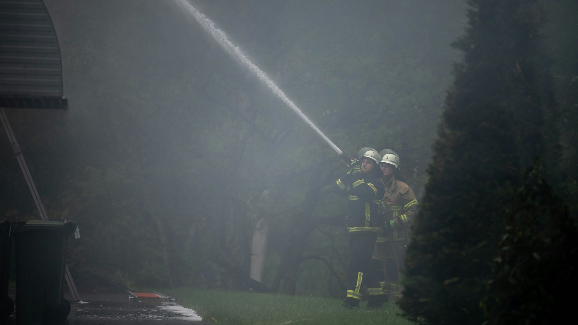 Das Bild zeigt zwei Feuerwehrleute, die die Fassade des Krematorium kühlen.