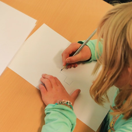 Ein Kind zeichnet etwas auf ein Blatt.