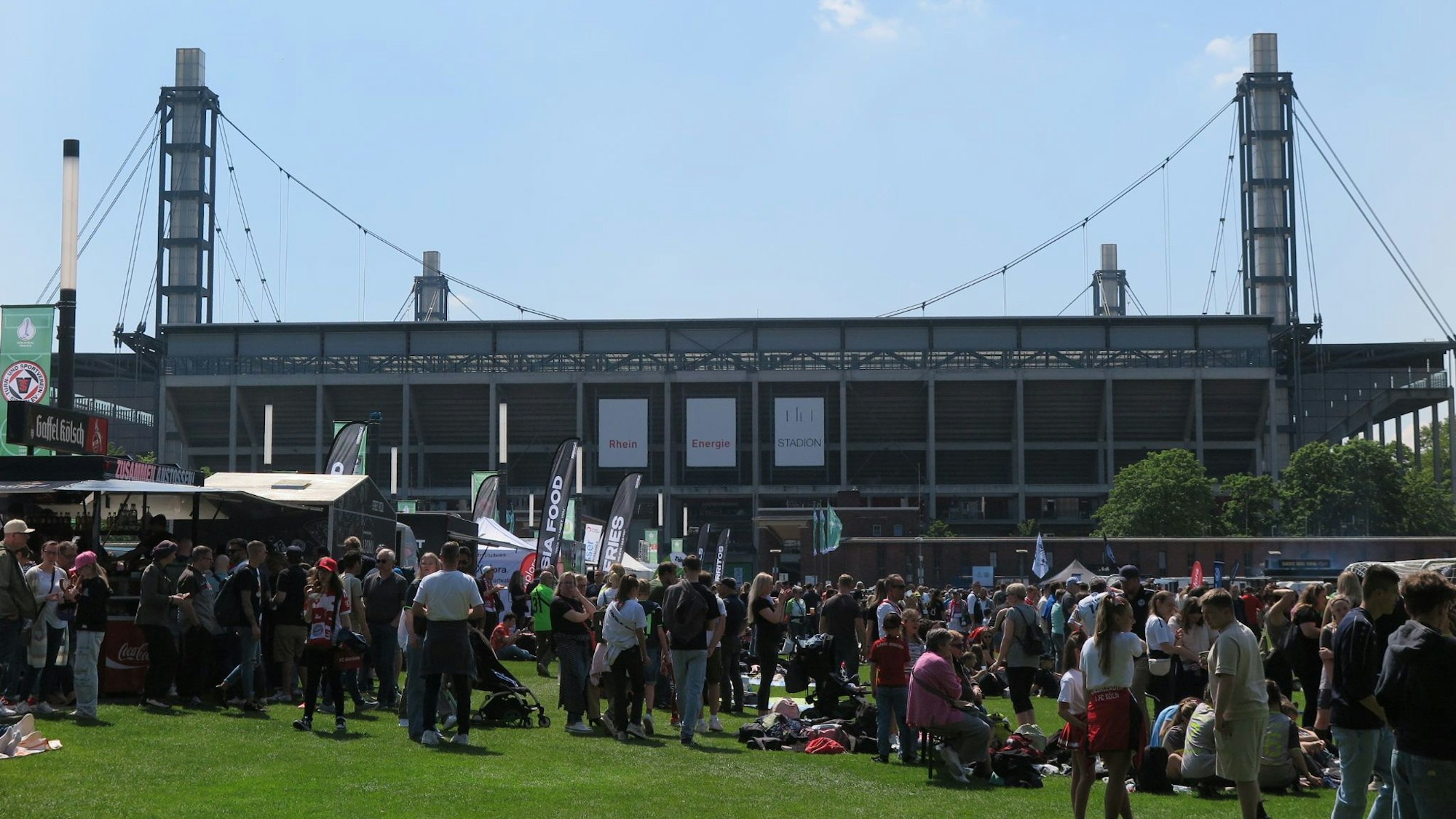 Menschen stehen auf der Wiese vor dem Rhein-Energie-Stadion in Köln-Müngersdorf