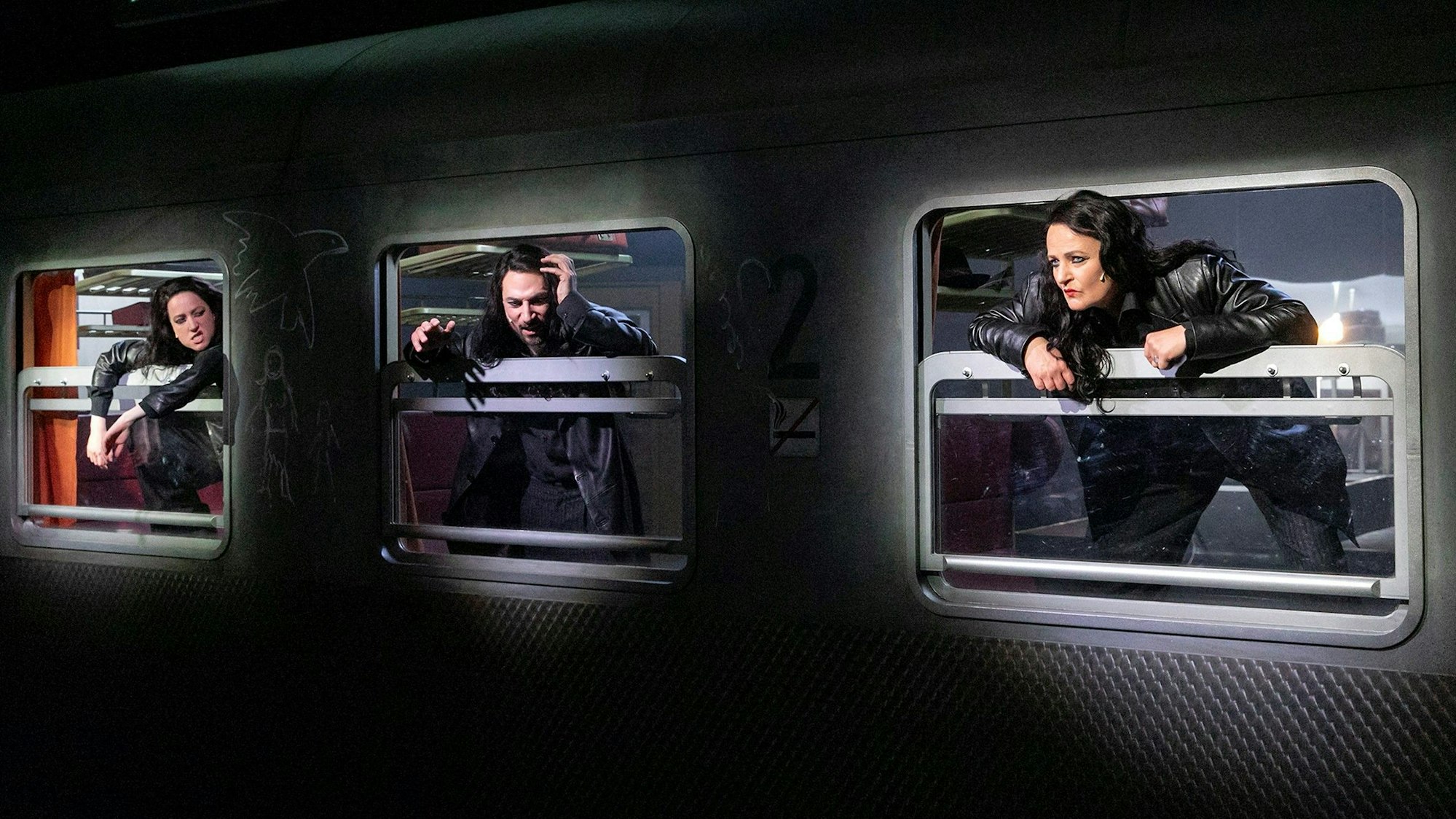 Kristin Steffen, Daron Yates und Michaela Steiger (v.l.) beugen sich aus den geöffneten Fenstern eines alten Bahnwaggons. Sie tragen schwarze Langhaar-Perücken und schwarze Lederjacken.