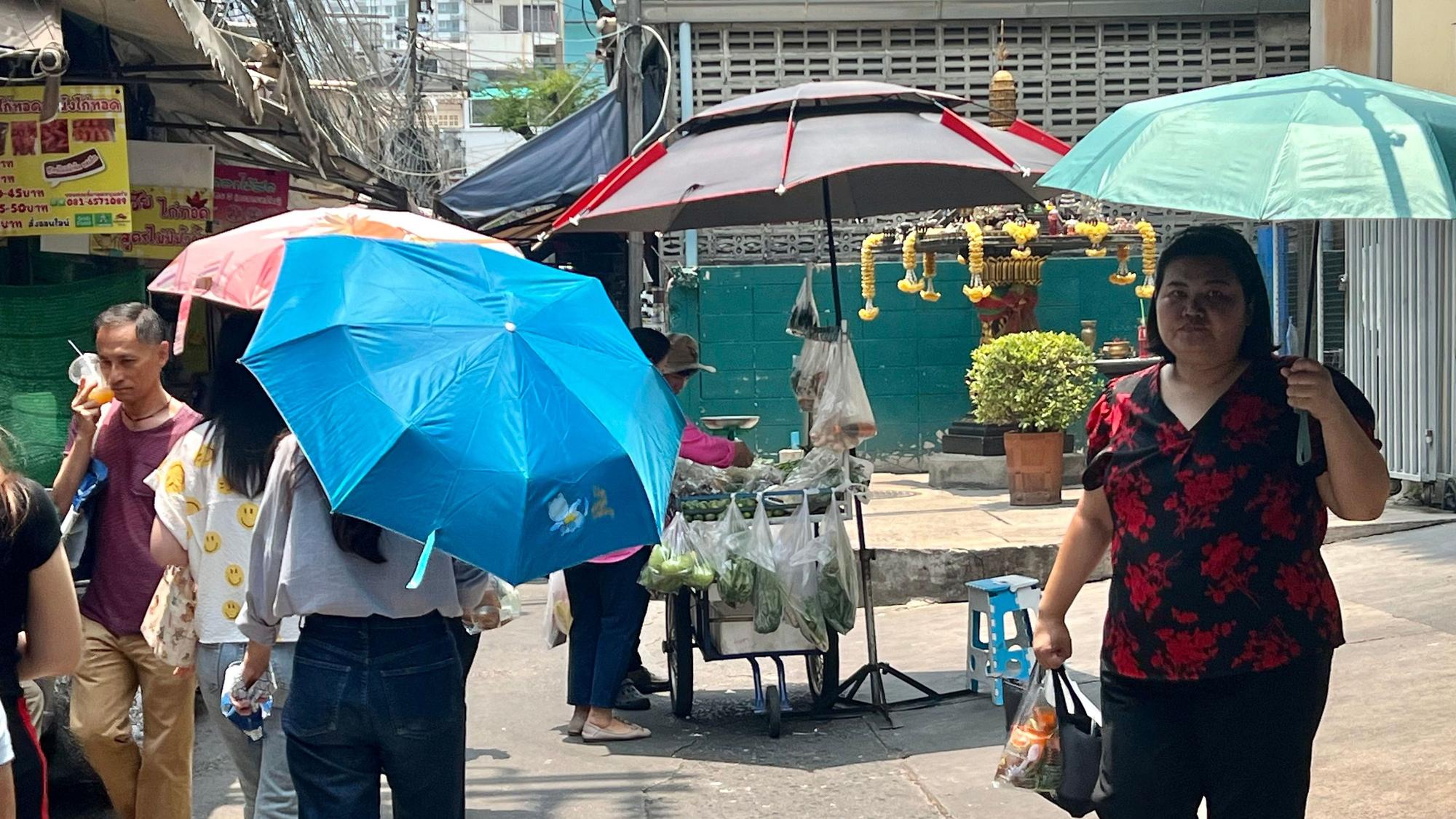 Thailand, Bangkok: Menschen schützen sich in Bangkok mit Schirmen vor der extremen Hitze und vor der Sonne.