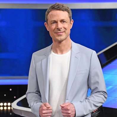 Moderator Alexander Bommes steht vor einer blauen Wand im Studio der ARD-Quizshow „Gefragt – Gejagt“.