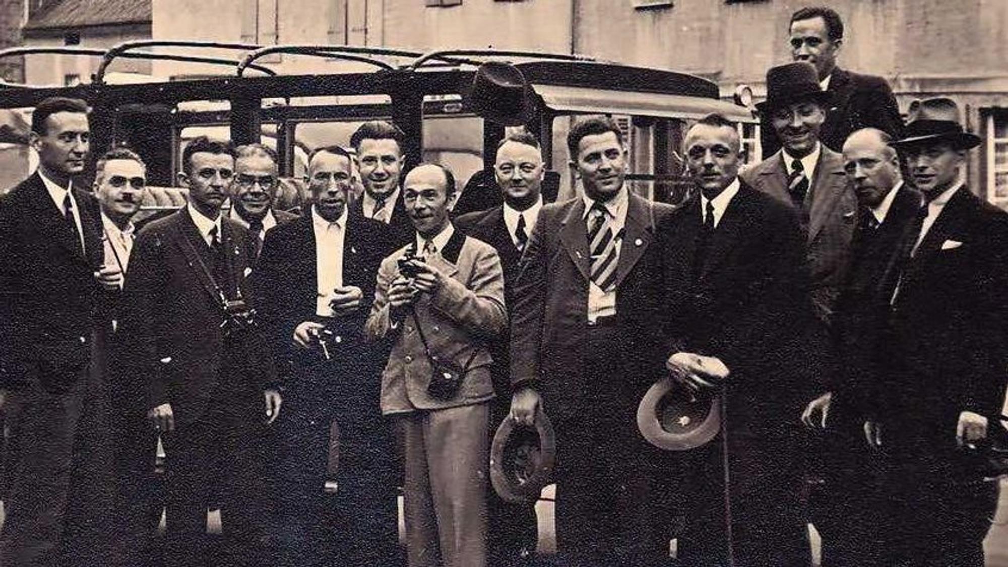 Auf einem historischen Bild stehen mehrere Männer vor einem Auto.