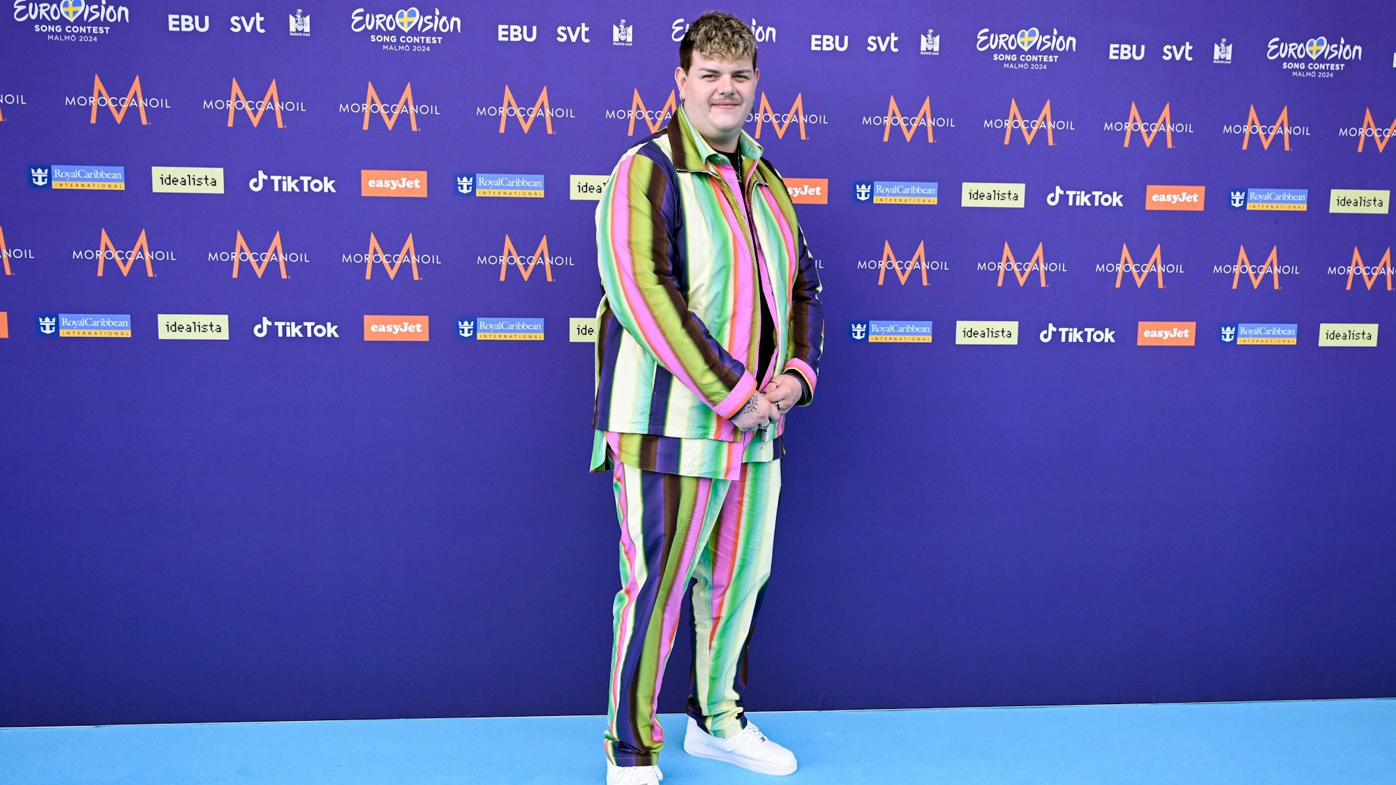 Isaak, der Deutschland repräsentiert, steht auf dem türkisfarbenen Teppich vor der Eröffnungszeremonie des 68. ESC in einem bunt gestreiften Outfit.