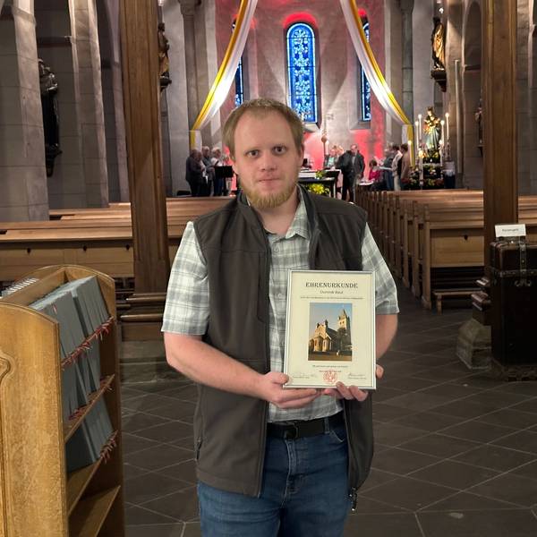Foto von Dominik Beul in einem Kirchenraum – mit Urkunde in den Händen.
