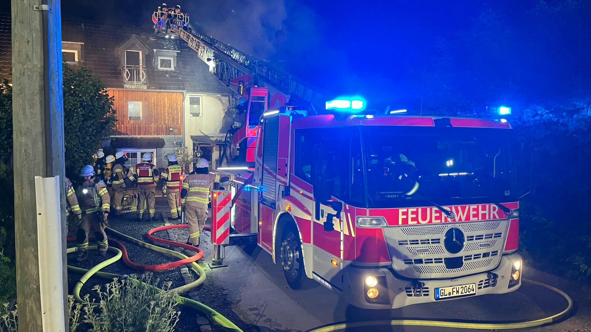 Eine Feuerwehrdrehleiter mit Blaulicht steht vor einem brennenden Haus.