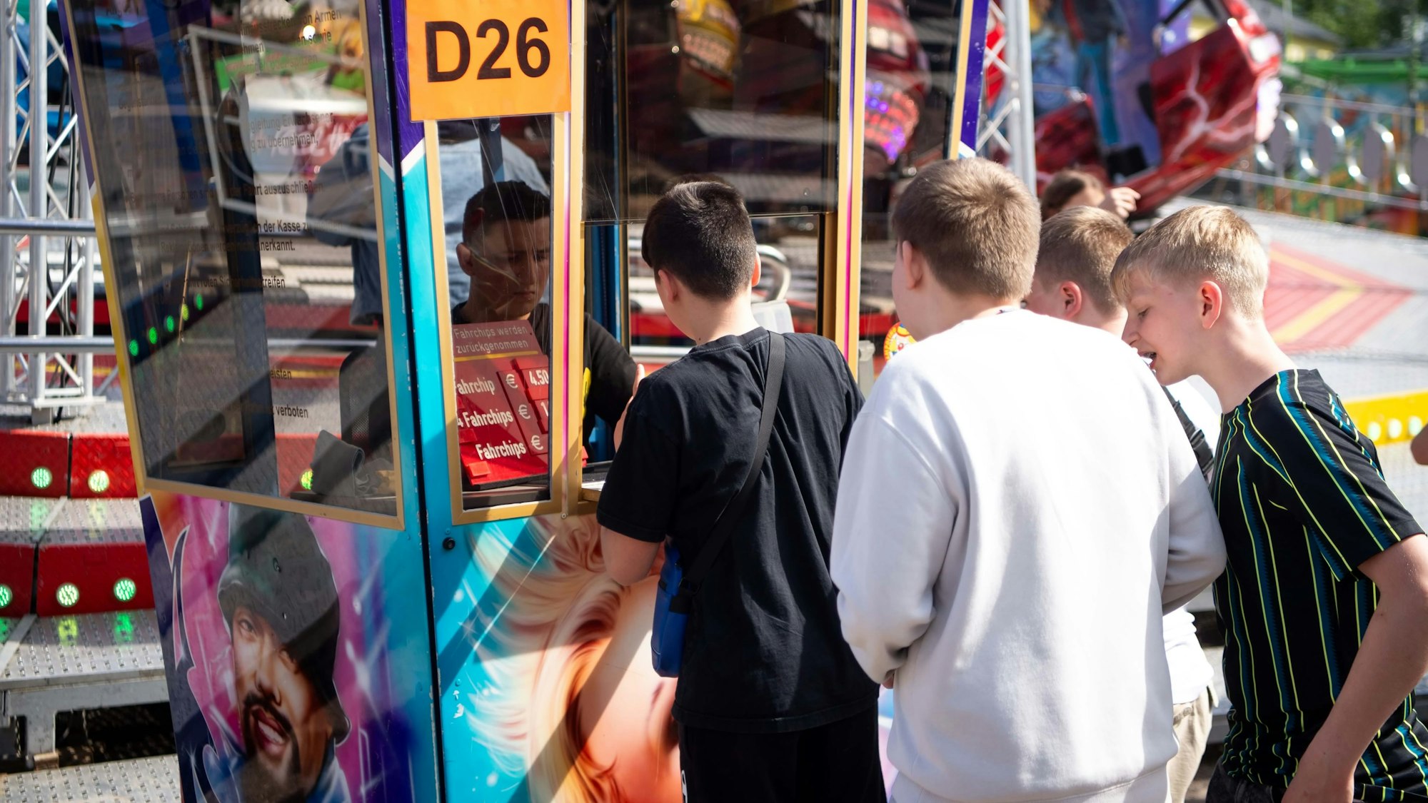 Das Bild zeigt vier Jugendliche, die sich an einem Fahrgeschäft Chips kaufen.