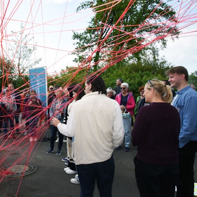 Blick auf ein netz aus roter Schnur, vor dem Menschen stehen.