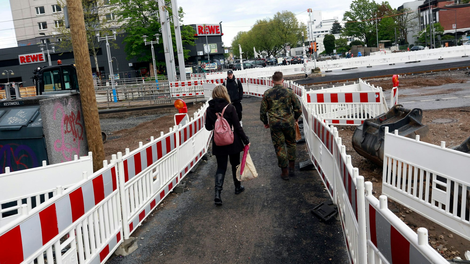 Passanten laufen zwischen Schutzbaken über eine Baustelle