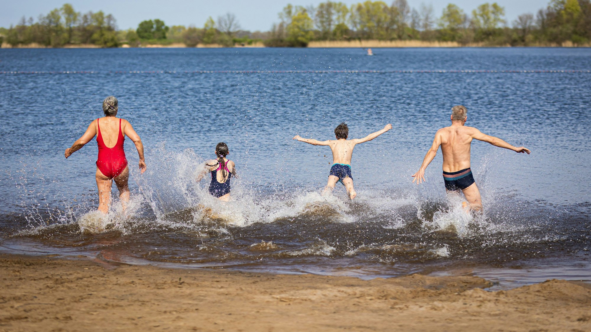 Eine Familie läuft bei sonnigem Wetter in einen Badesee.