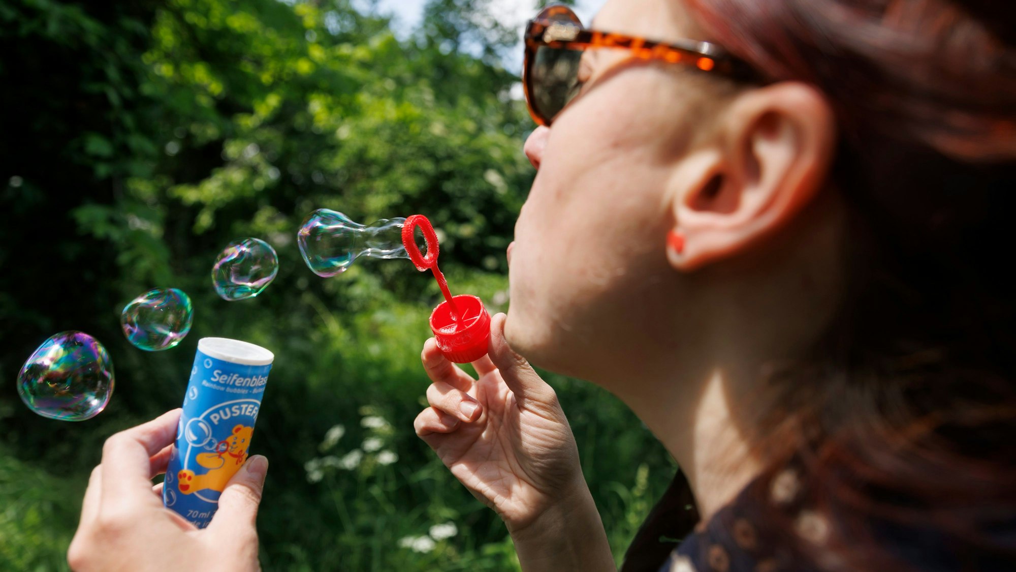ILLUSTRATION - 24.05.2023, Baden-Württemberg, Stuttgart: Eine Frau bläst Seifenblasen mit einem Spielzeug der Marke Pustefix. Pustefix feiert in diesem Jahr sein 75-jähriges Bestehen. Mit Seifenblasen-Spielen made in Germany wurde die Firma berühmt. Der Markt ist in der Branche aber hart umkämpft. Foto: Julian Rettig/dpa +++ dpa-Bildfunk +++