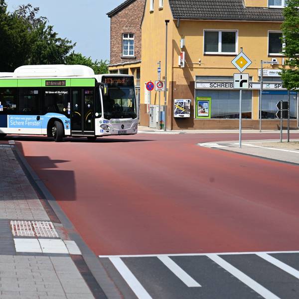 Auf dem Foto ist die Carl-Schurz-Straße in Erftstadt-Liblar zu sehen. Ein Bus fährt um die Ecke. Die gesamte Kreuzung ist mit einem roten Belag versehen.