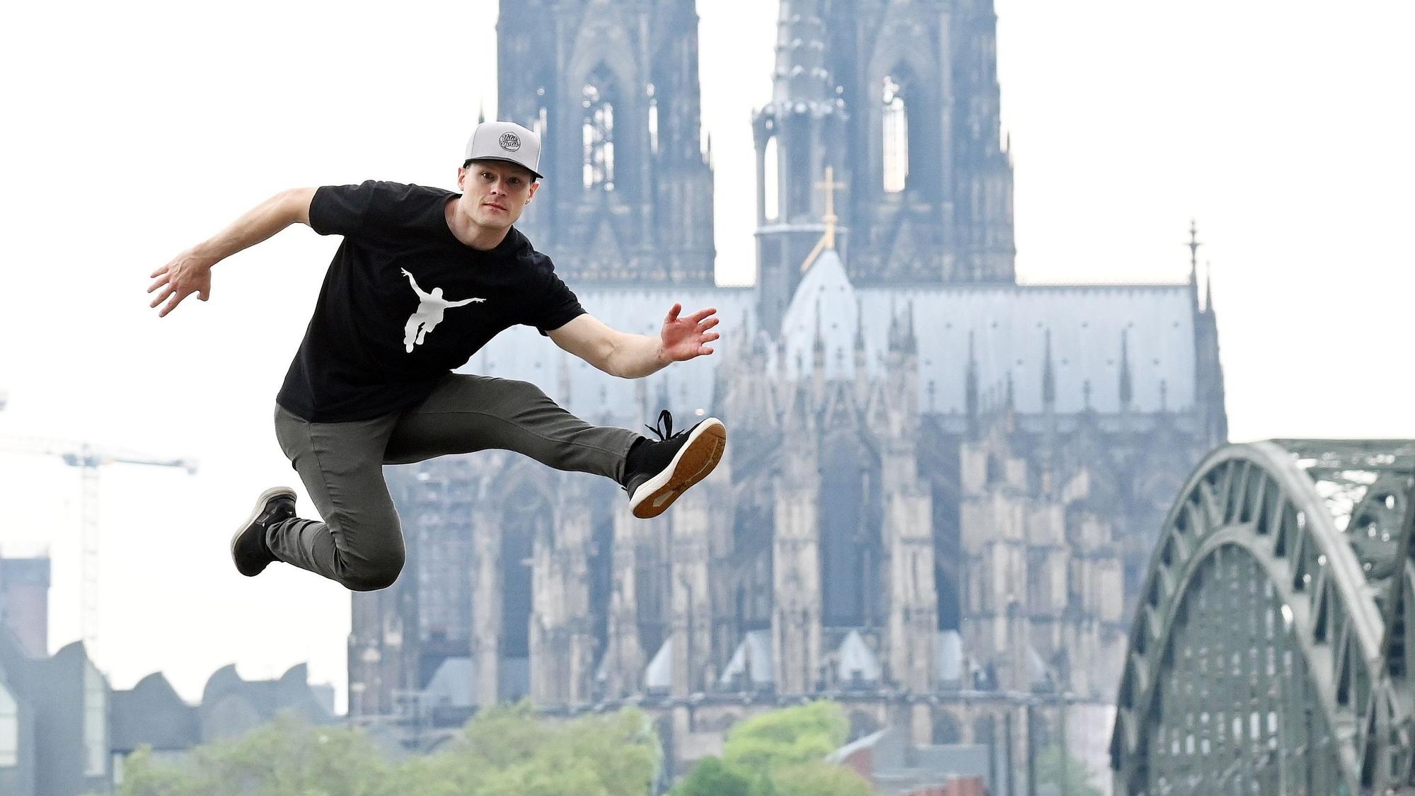 Ein Mann springt vor dem Dom im Hintergrund hoch in die Luft.