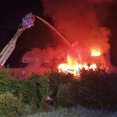 Die Feuerwehr löscht von einer Drehleiter aus ein in Flammen stehendes Haus.