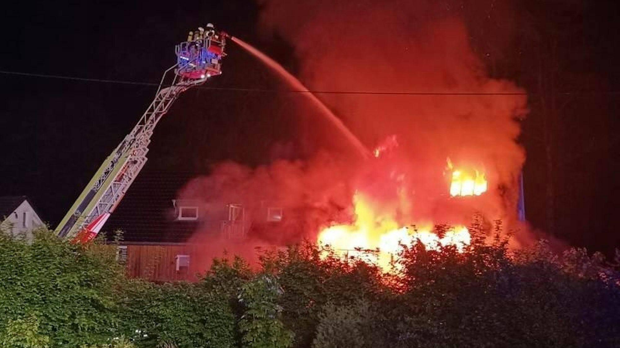 Von einer Feuerwehrleiter wird ein lichterloh brennendes Haus gelöscht.