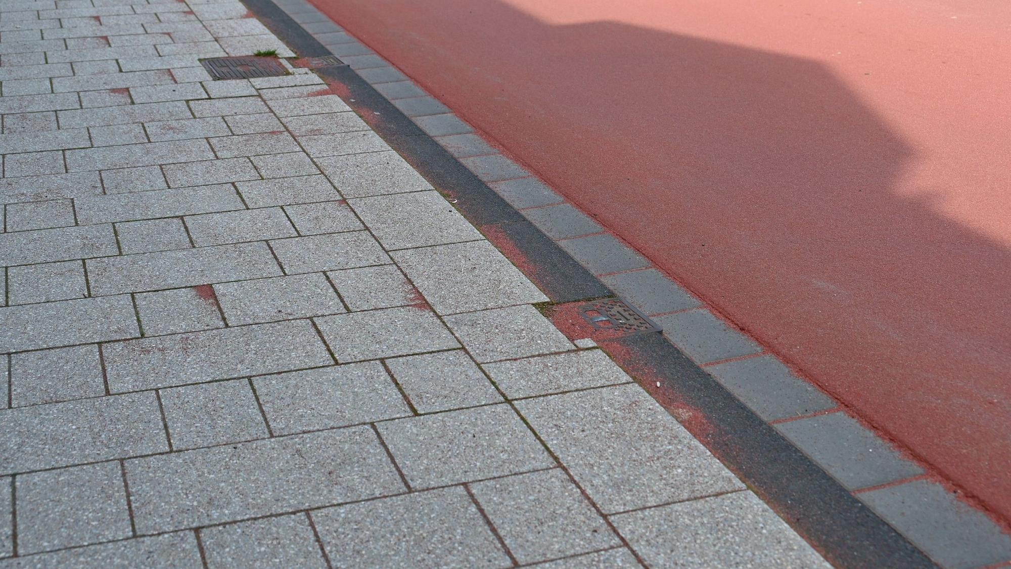 Das Foto zeigt den Abrieb des roten Belags auf dem Bürgersteig.