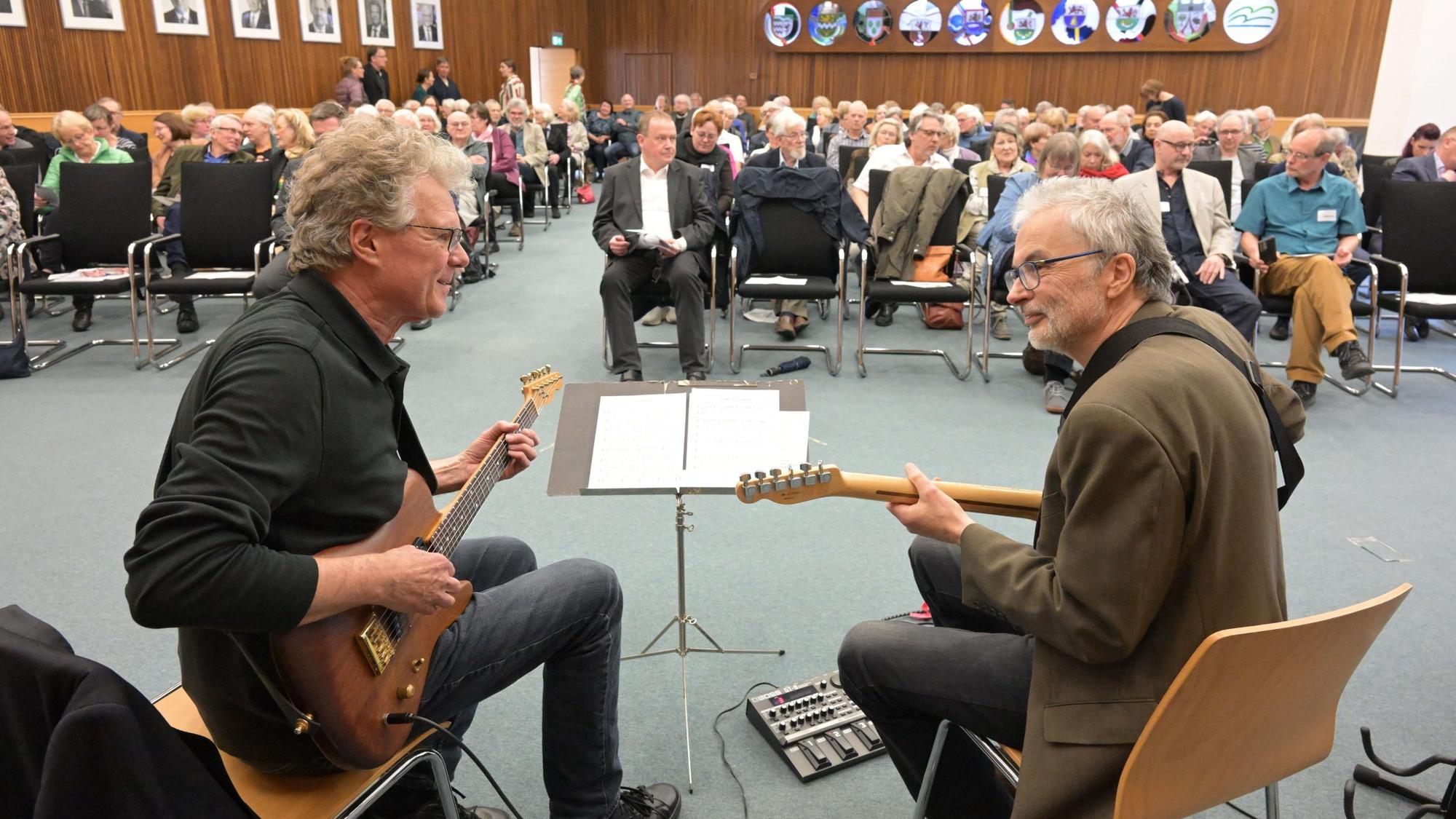 Zwei Männer spielen Gitarre vor Publikum.