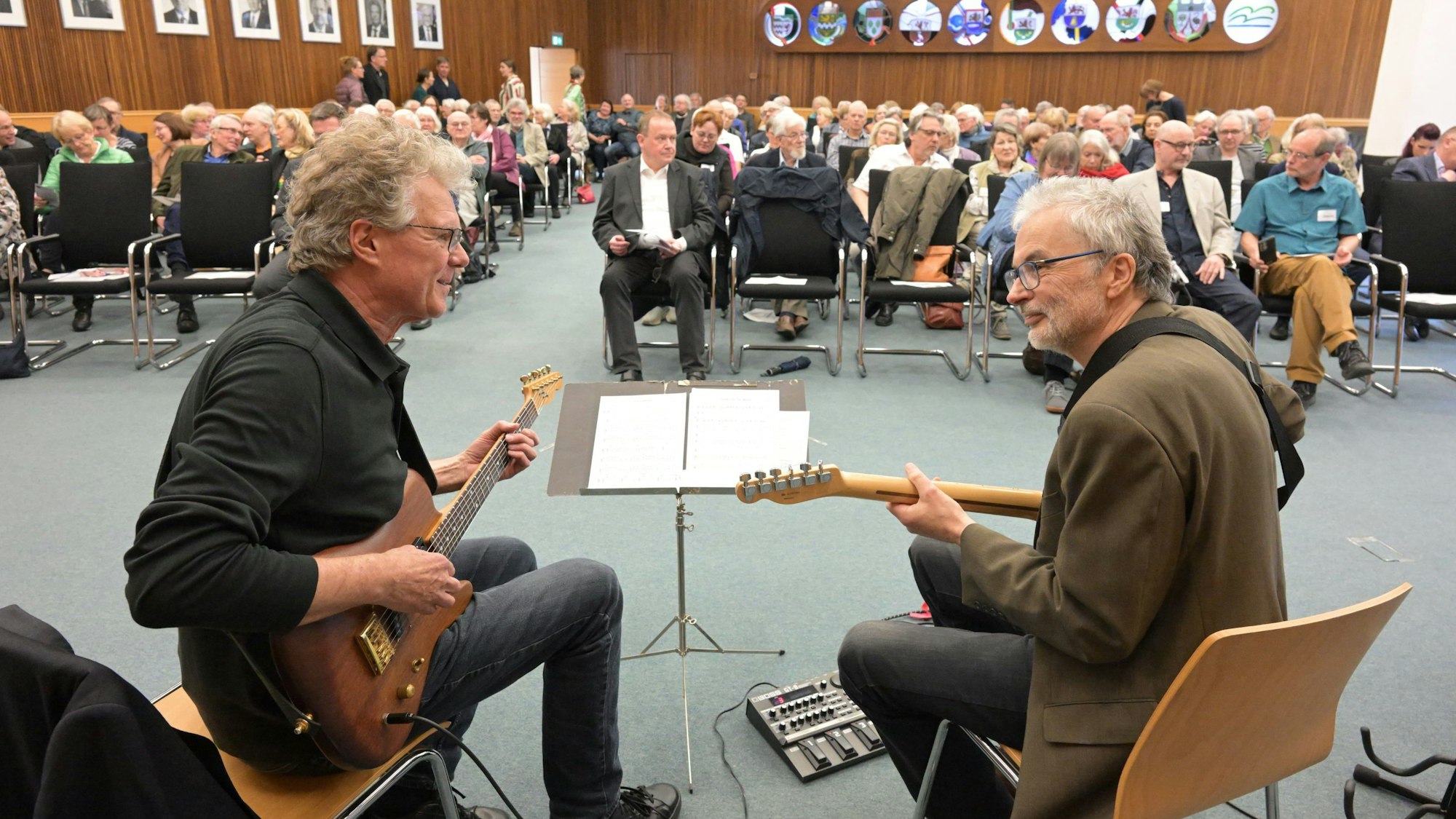 Zwei Männer spielen Gitarre vor Publikum.