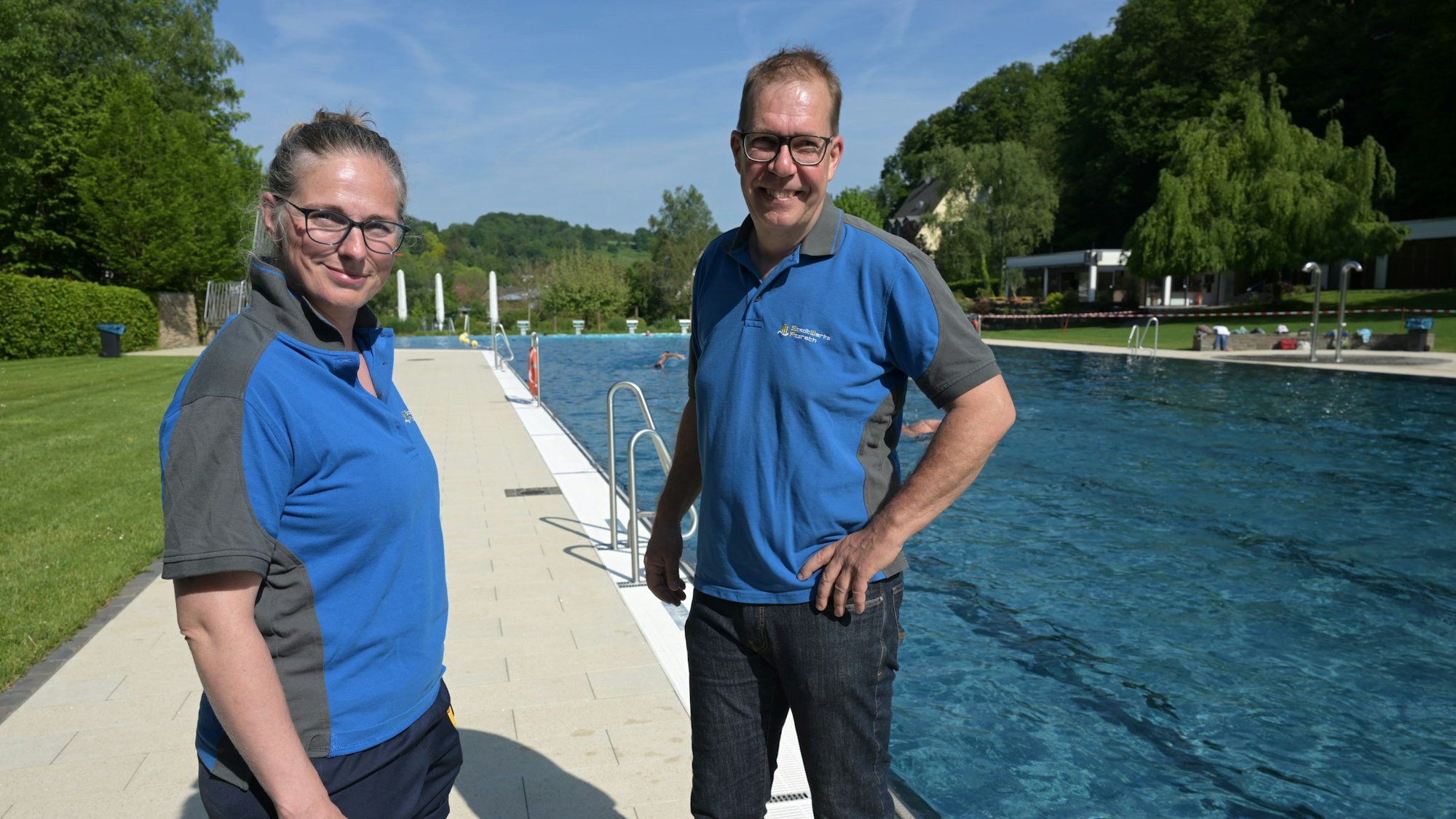 Eine Bademeisterin und ein Bademeister stehen am Rand eines Schwimmbeckens im Freibad.
