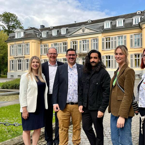 Drei Männer und drei Frauen stehen vor einem Schloss.