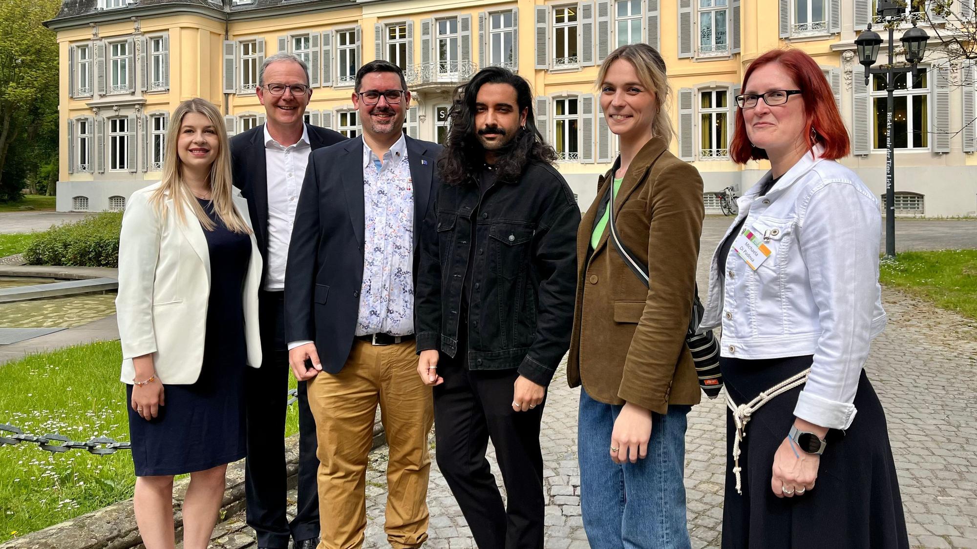 Drei Männer und drei Frauen stehen vor einem Schloss.