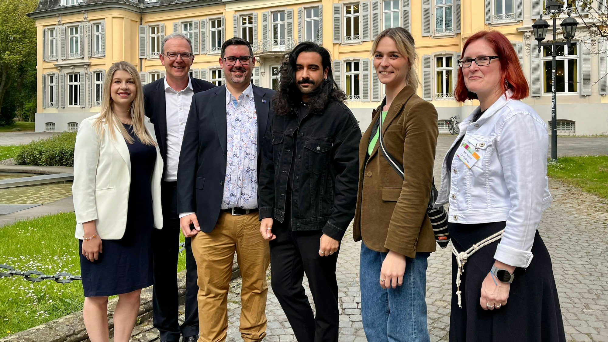 Drei Männer und drei Frauen stehen vor einem Schloss.
