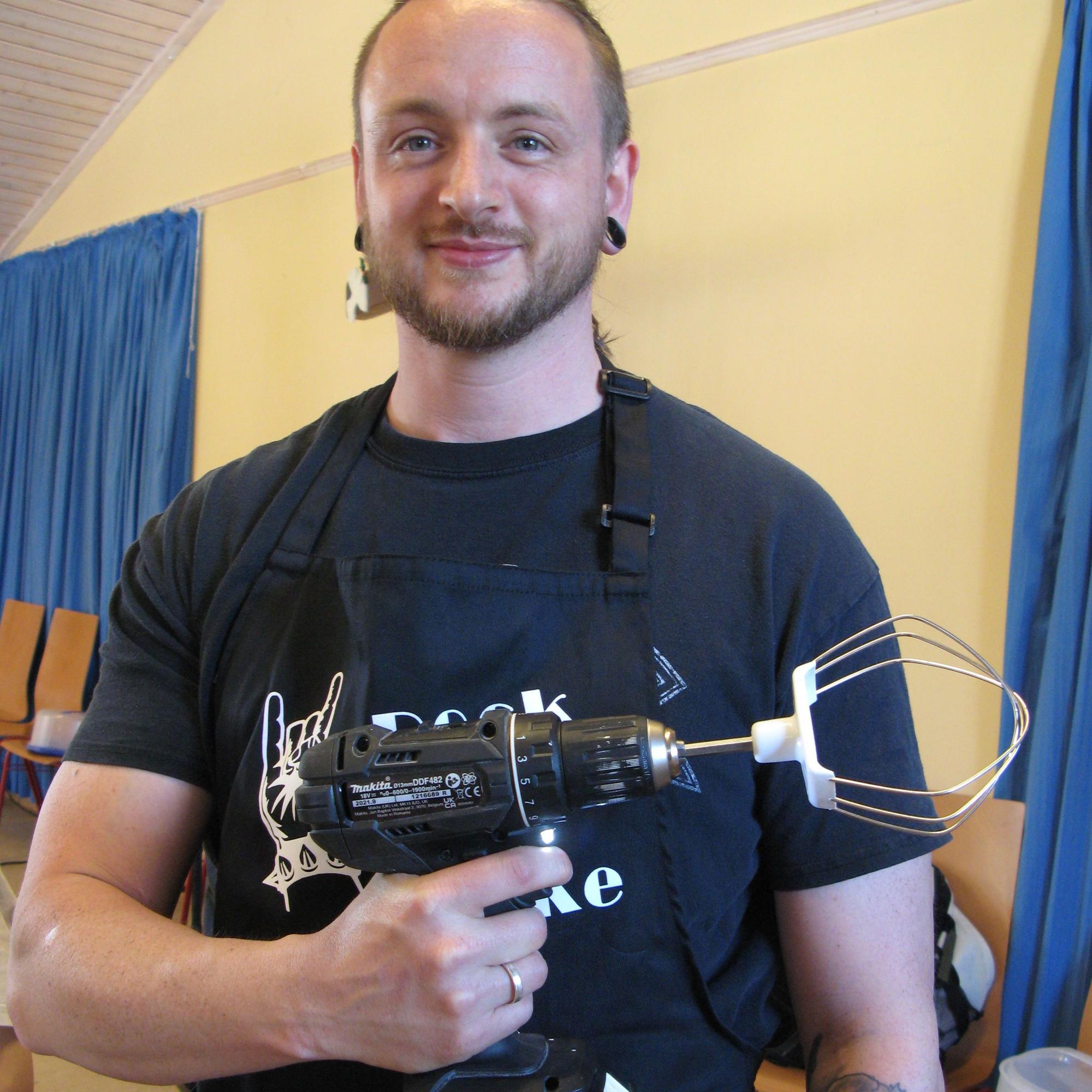 Ein Mann hält einen Akkuschrauber, der Aufsatz ist ein Teigrührer.