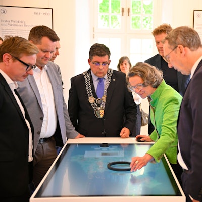 Blick auf eine Gruppe von Menschen an einer digitalen Infotafel
