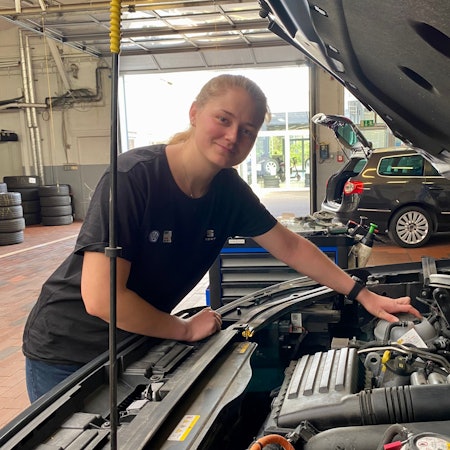 Eine junge Frau an einer geöffneten Motorhaube.