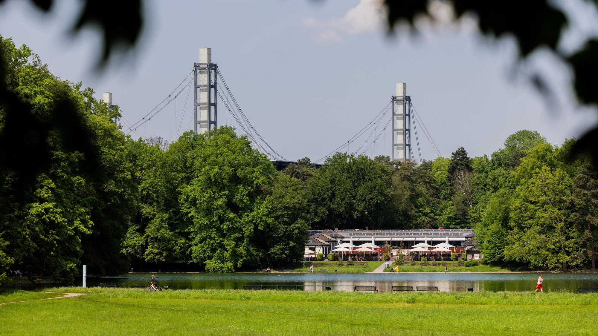 ARCHIV - 02.05.2024, Nordrhein-Westfalen, Köln: Menschen genießen das sonnige Wetter am Adenauer Weiher im Stadtwald vor der Kulisse des RheinEnergieStadions.