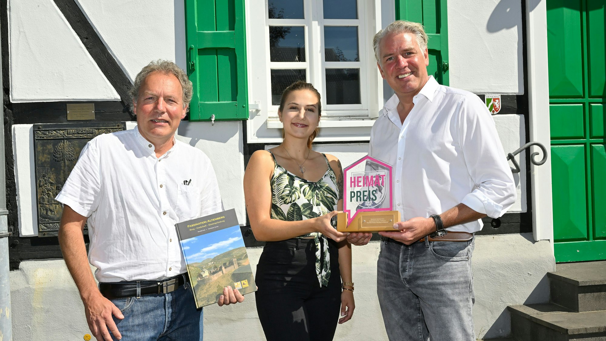 Randolph Link, Diana Link, und Bürgermeister Robert Lennerts (rechts) bei der Verleihung des Odenthaler Heimatpreises. Dahinter ein bergisches Fachwerkhaus.