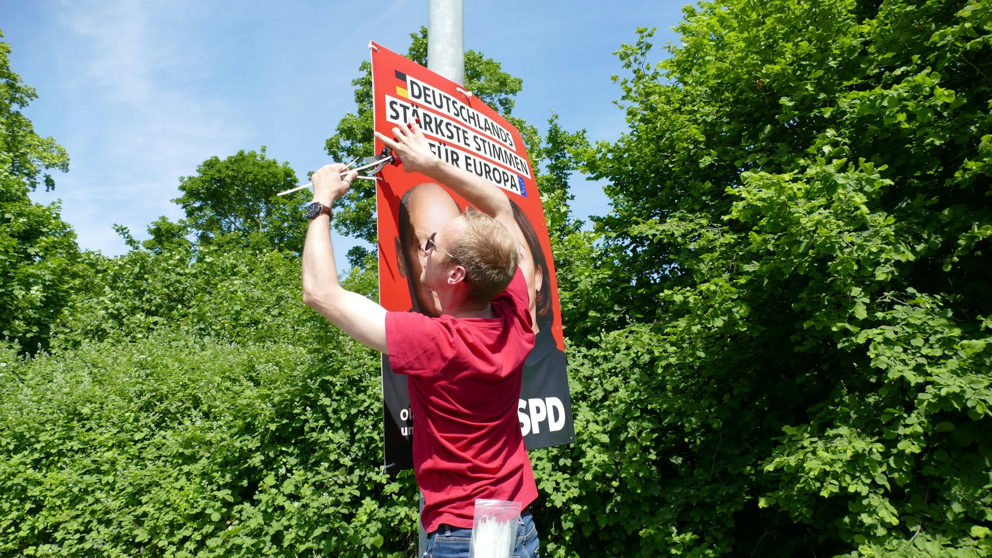 Michael Richter, der Kreisgeschäftsführer der SPD in Bonn und dem Rhein-Sieg-Kreis, hängt an einem Laternenmast ein Plakat zur Europawahl auf.