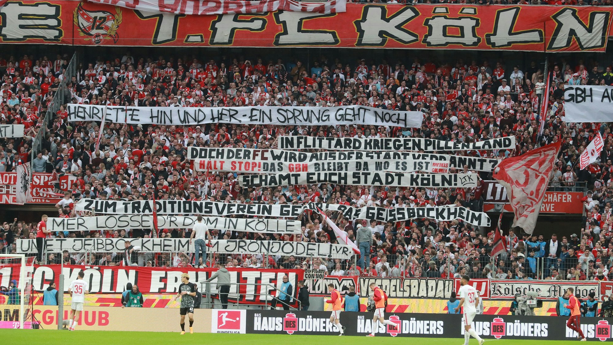 In der Südkurve des Kölner Stadions halten Fans zahlreiche Banner in die Höhe. Auf einem ist zu lesen „Henriette Hin und Her – Ein Sprung geht noch“, der auf einen Richtungswechsel von OB Henriette Reker in der Frage der Geißbockheim-Erweiterung im Grüngürtel anspielt.