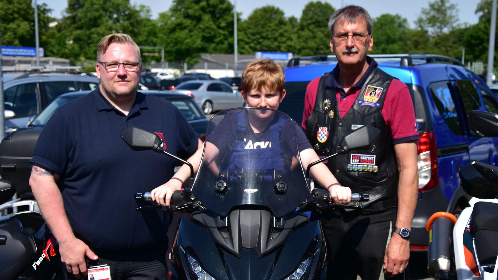 Nachwuchs-Feuerwehrmann Finn sitzt bei der Spendenaktion der Biker der Bundespolizei auf einem Motorrad, eingerahmt von den beiden Bikern Markus Mattern (l.) und Dirk Stenzel (r.).