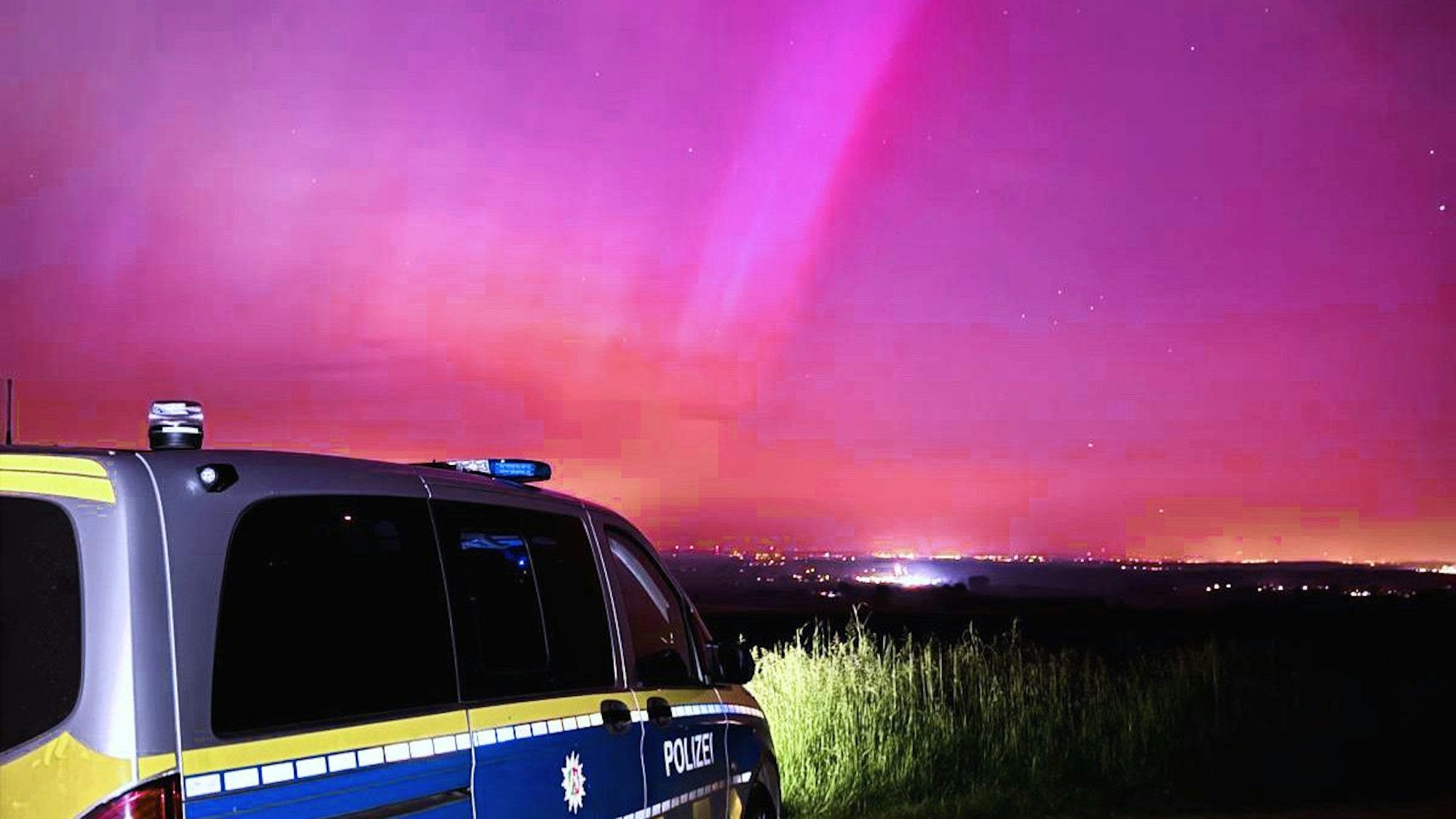 Vor dem rötlich leuchtenden Himmel steht ein Polizeiauto.