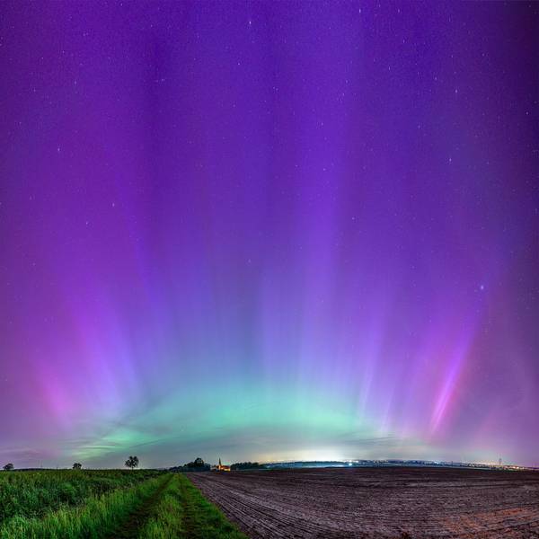 Über einem Feld und einem Kirchturm schillert der Himmel grün und violett.