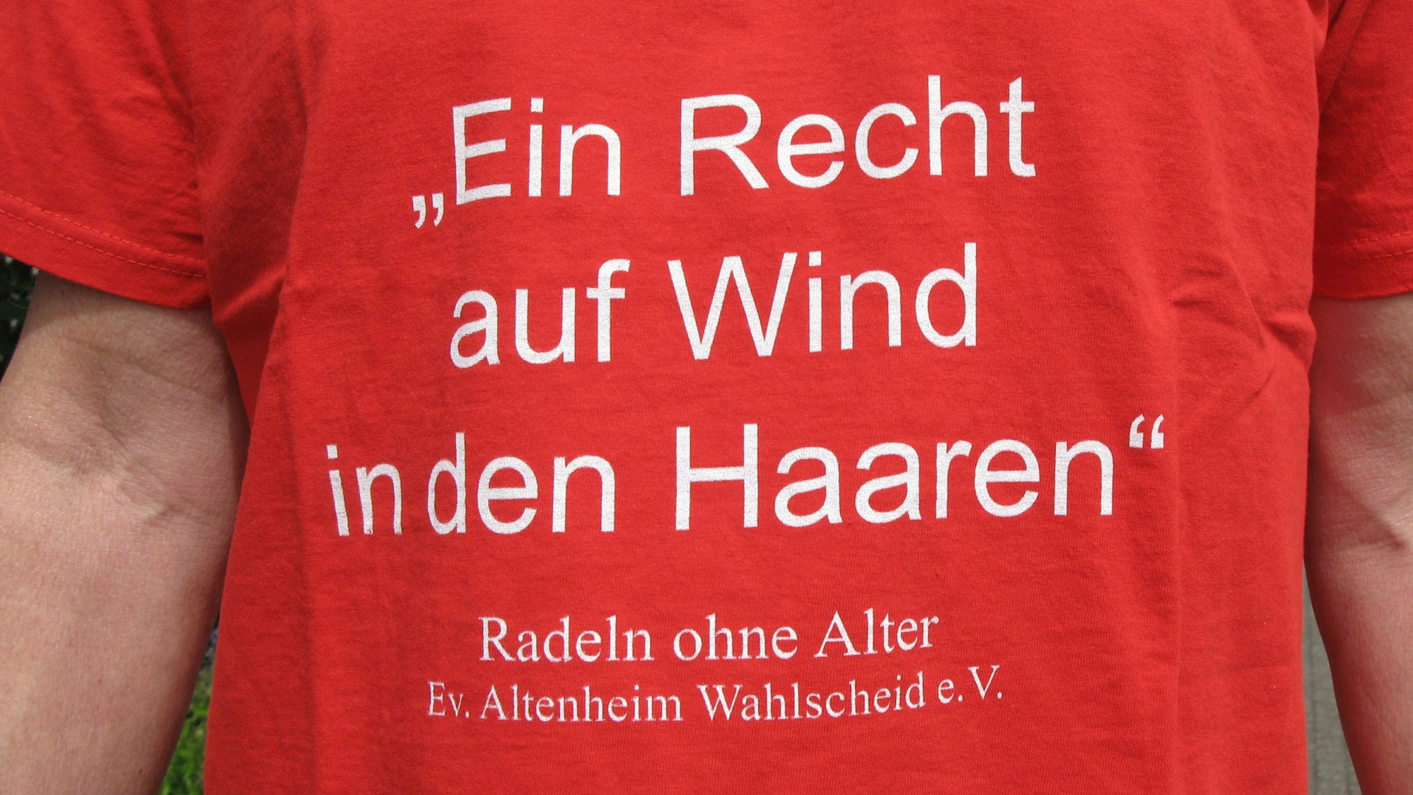 Auf einem roten T-Shirt steht „Ein Recht auf Wind in den Haaren – Radeln ohne Alter, Evangelisches Altenheim Wahlscheid e.V.“