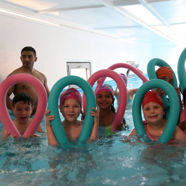 Acht Kinder posieren mit ihren Schwimmnudeln im Wasser.
