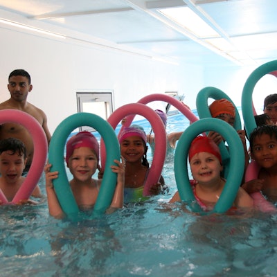 Acht Kinder posieren mit ihren Schwimmnudeln im Wasser.