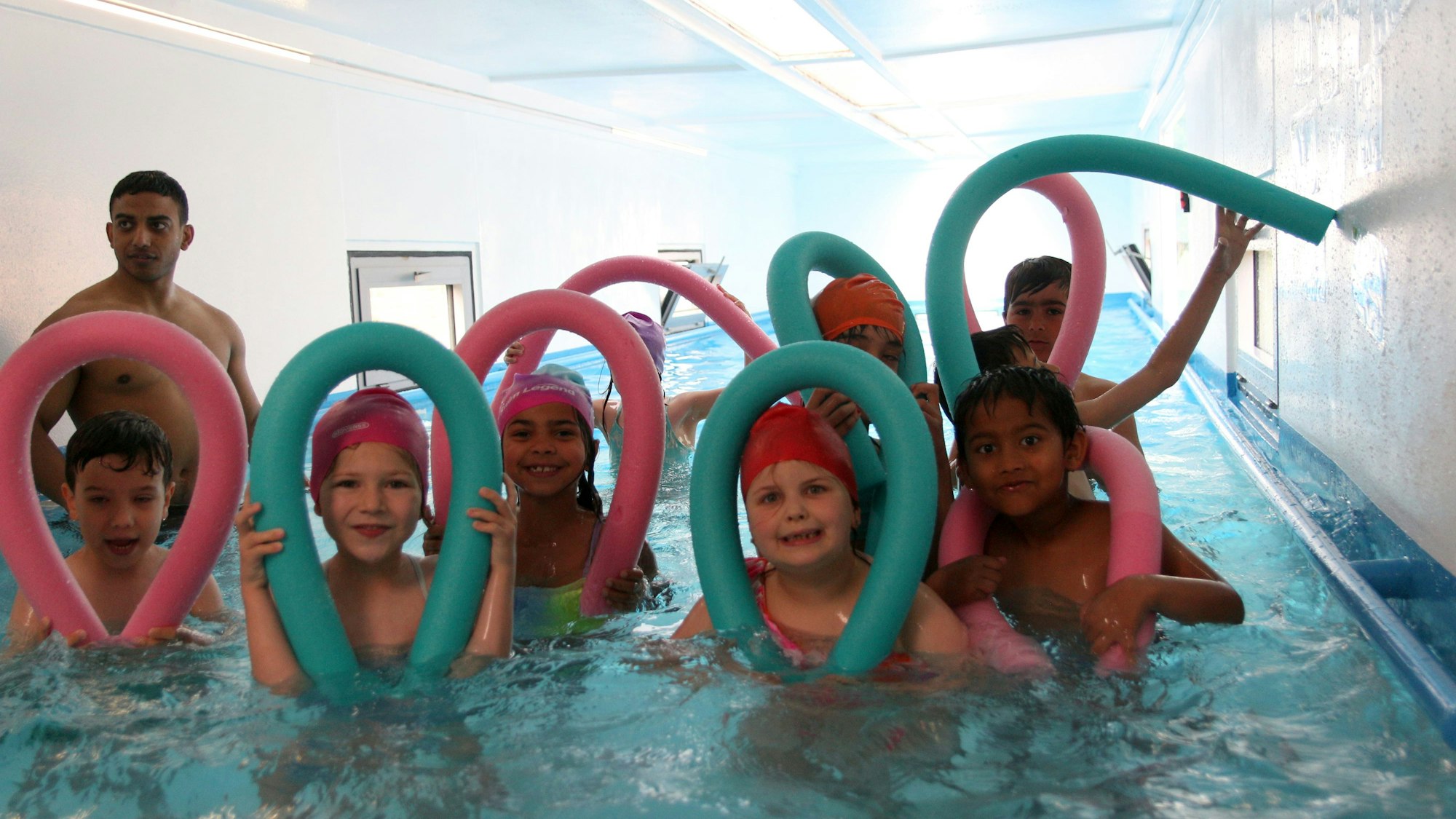 Acht Kinder posieren mit ihren Schwimmnudeln im Wasser.
