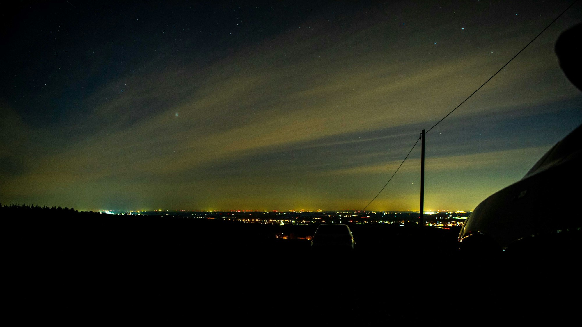 Am unteren Bildrand sind die Lichter der Stadt zu sehen, darüber grünliche Streifen im Himmel.