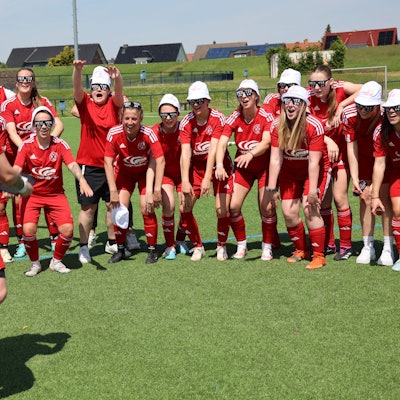 Fußballspielerinnen tragen weiße Kappen und jubeln.