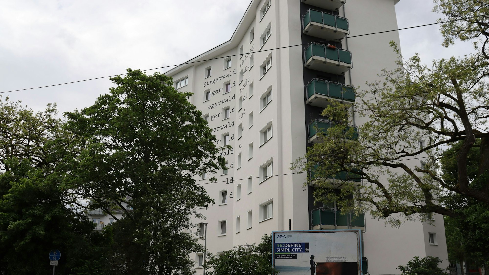 Ein weißes Hochhaus mit grün gestrichenen Balkonen, umgeben von Bäumen, in Mülheims Stegerwaldsiedlung. Foto von Uwe Schäfer