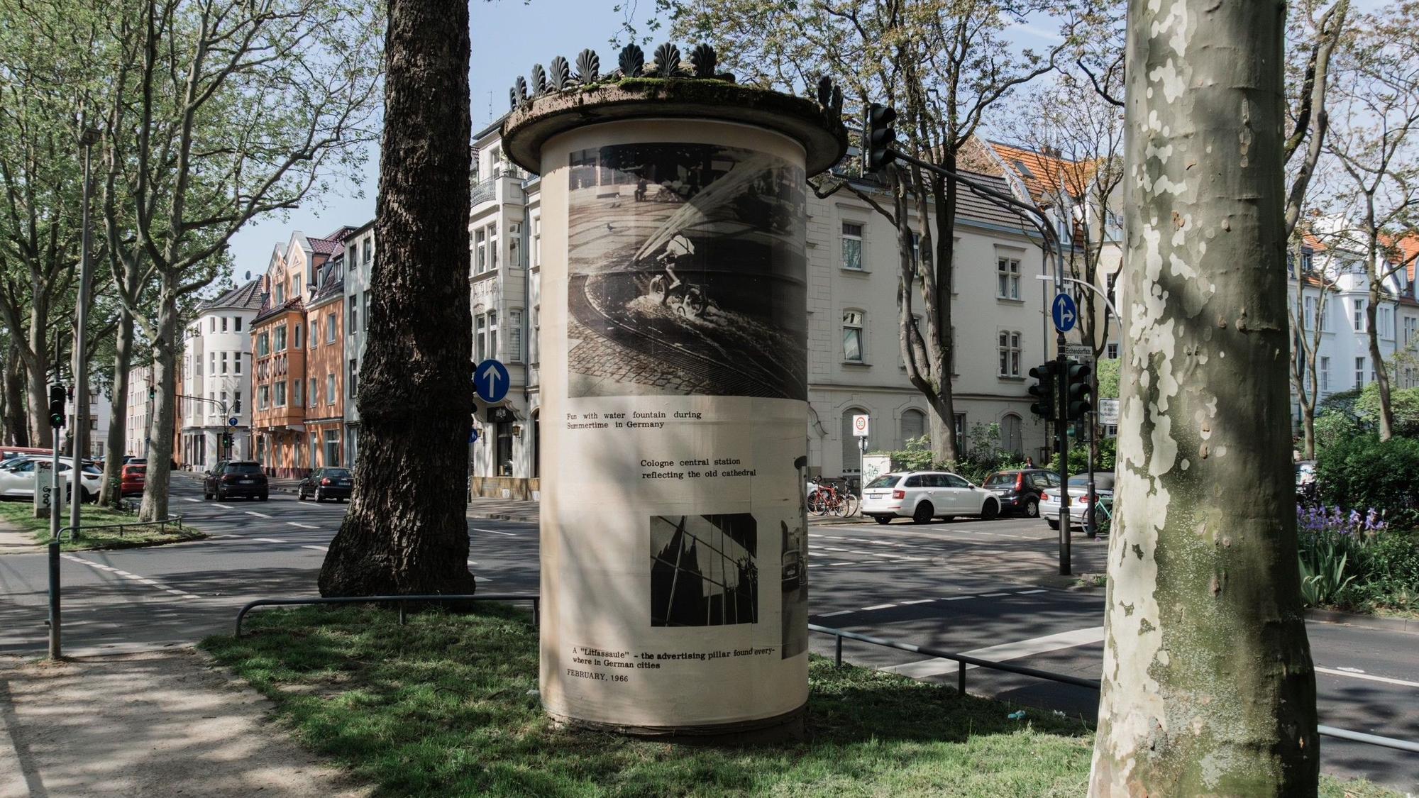 Zu sehen ist eine Litfaßsäule auf einem Grünstreifen.