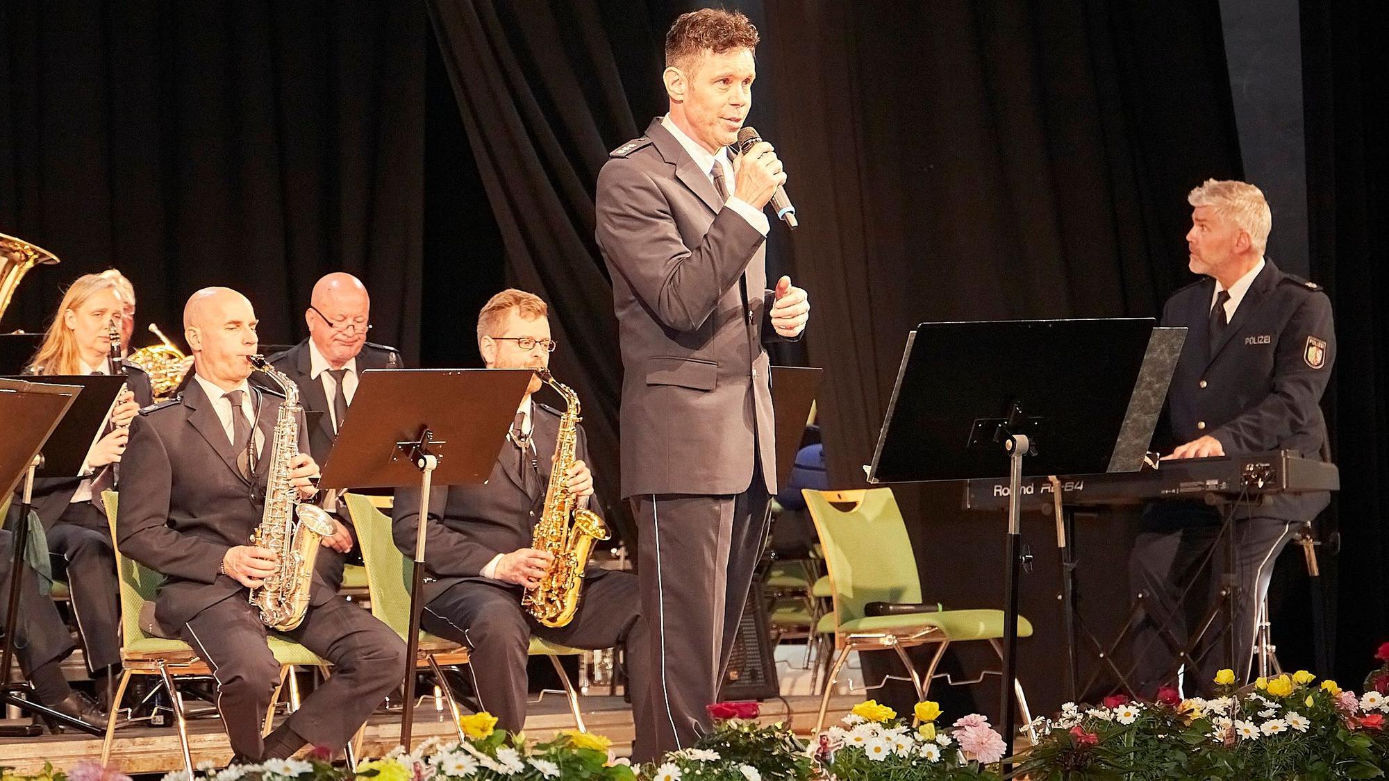 Musiker in Polizeiuniform geben im Gemünder Kursaal ein Konzert. Oliver Schmitt hält ein Mikrofon in der Hand und singt.