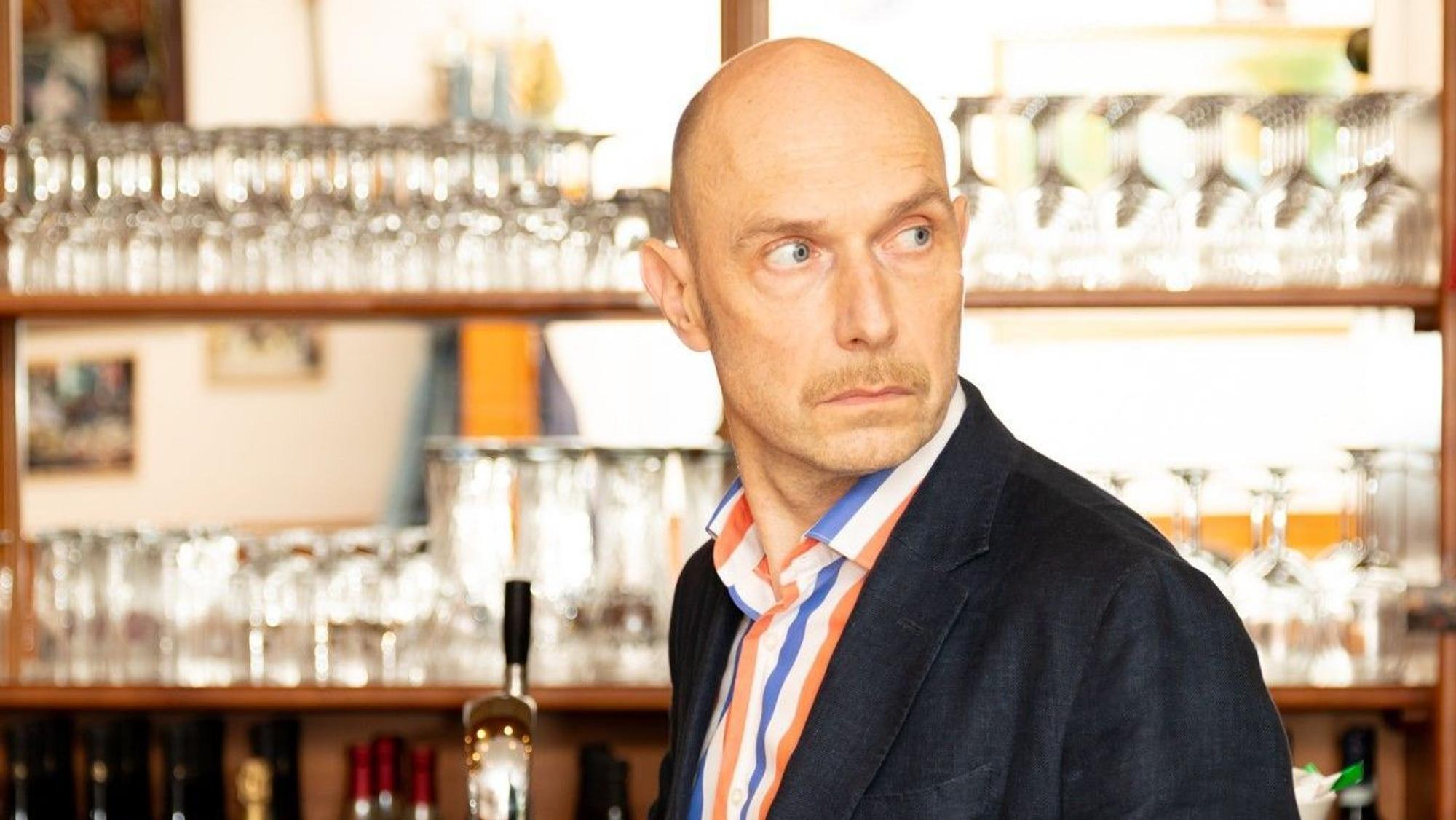 Eric Pfeil steht an einer italienischen Kaffeebar. Er trägt ein dunkles Jackett und ein gestreiftes Hemd.