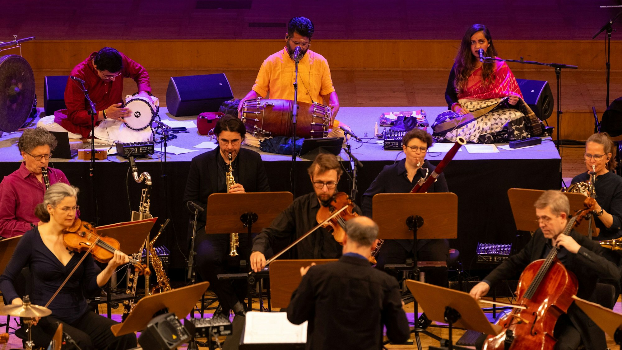 Auf dem Foto zu sehen ist im Vordergrund das WDR-Orchester, im Hintergrund das indische Trio an Trommeln und Percussion-Instrumenten.
