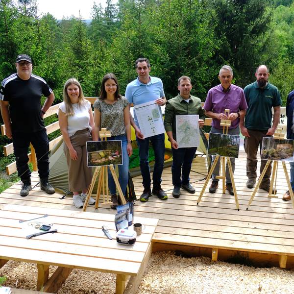 Vertreter der beteiligten Kommunen, des Naturparks Nordeifel und der Nordeifel Tourismus GmbH stehen auf einer Holzplattform im Wald.
