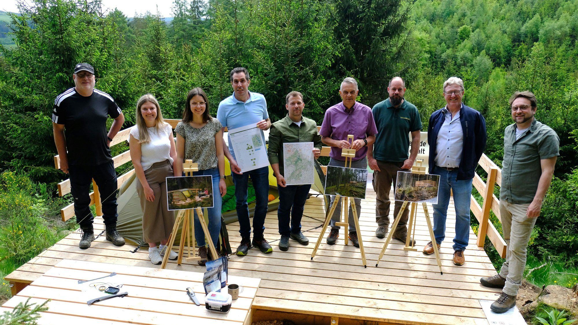 Vertreter der beteiligten Kommunen, des Naturparks Nordeifel und der Nordeifel Tourismus GmbH stehen auf einer Holzplattform im Wald.