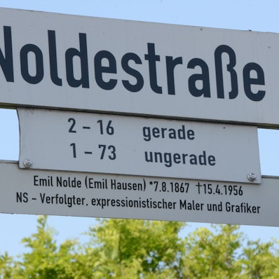 Das Bild zeigt ein Straßenschild mit der Aufschrift Noldestraße und einem Info-Hinweis darunter.